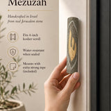 Person holding a handcrafted Jerusalem stone mezuzah with a prominent gold Shin letter.