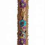 Intricate handmade Mezuzah decorated with colorful sequins and stones, mounted on a clean white background with soft reflection.