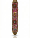 Pink handmade Mezuzah decorated with sequins and stones, crafted by Israeli artist Eva Mishaan, shown on a white studio background with soft reflection.