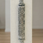 A high-angle shot of the traditional silver mezuzah affixed to a smooth, light-colored stone wall