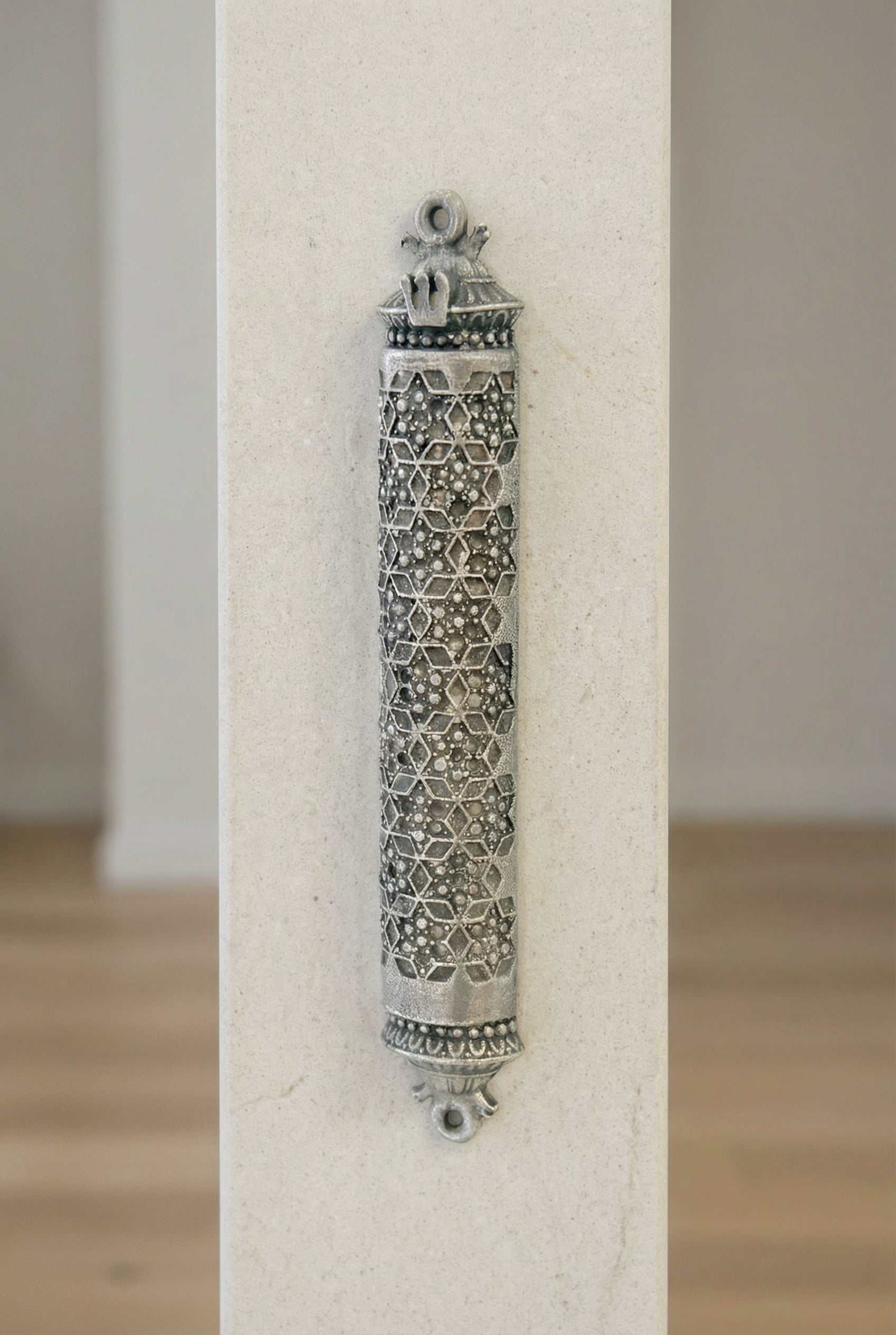 A high-angle shot of the traditional silver mezuzah affixed to a smooth, light-colored stone wall