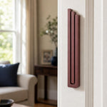 Realistic image of the exact modern burgundy pyramid mezuzah mounted vertically on a doorpost in a residential entryway, showing precise design and scale.