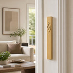 Eternal Flame Gold Aluminum Mezuzah mounted vertically on a residential doorpost, positioned within the lower third, showing its gold finish and Hebrew emblem.