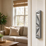 Silver geometric mezuzah mounted vertically on a residential doorpost, in a warm home entryway setting.