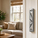 Silver geometric mezuzah mounted vertically on a residential doorpost, in a warm home entryway setting.
