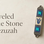Jeweled Blue Stone pewter mezuzah case mounted on a light wall, featuring an antique silver-tone finish, bright turquoise square stones, rows of blue crystals, ornate detailing, and a jeweled Hebrew Shin. This decorative blue Jewish mezuzah case adds rich color and traditional Judaica style to a home doorway