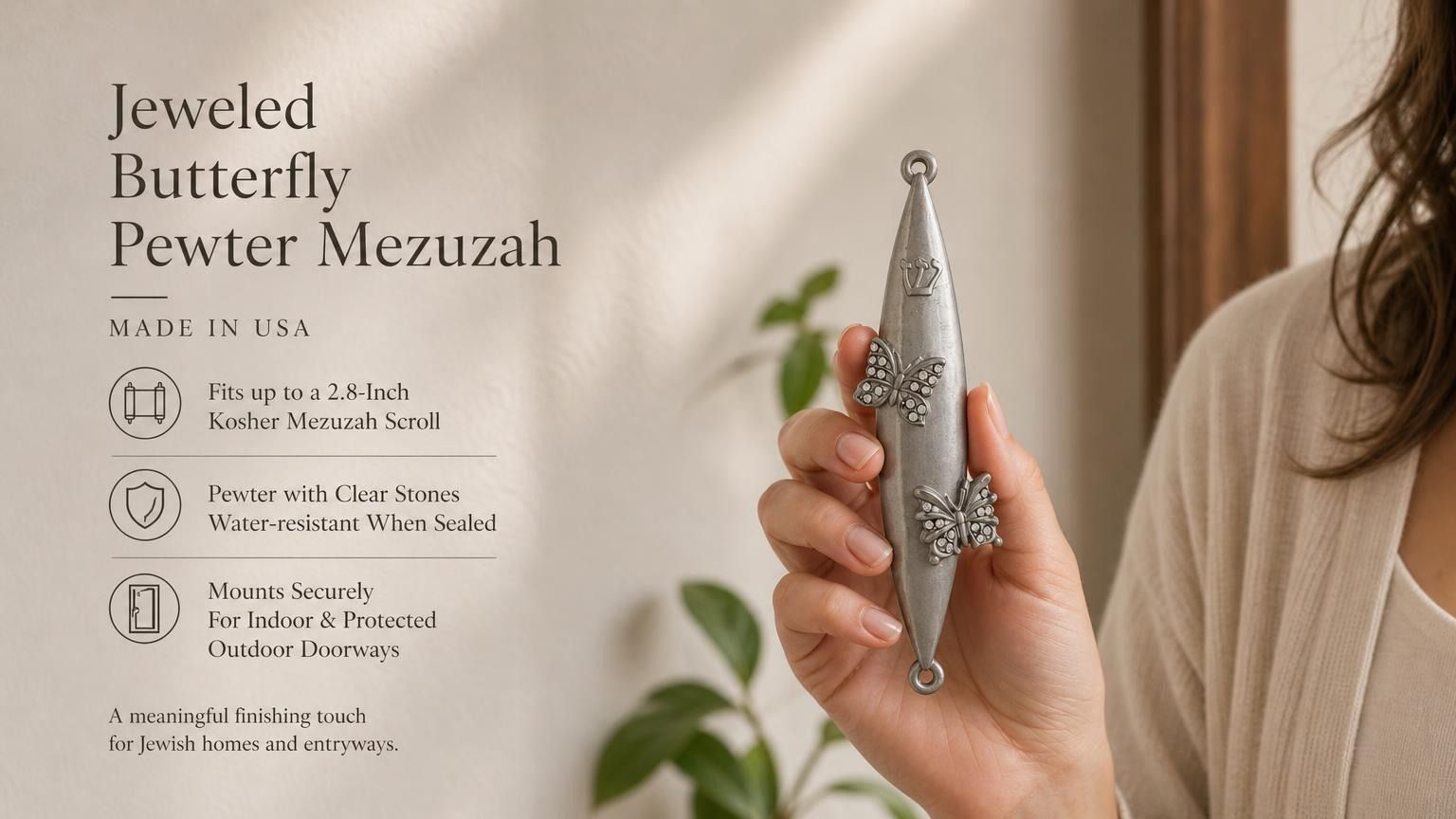 Jeweled Butterfly pewter mezuzah case held in a woman’s hand, featuring an elongated silver-tone body with two raised butterfly designs accented by clear sparkling stones and a Hebrew Shin near the top. This decorative Jewish mezuzah case fits up to a 2.8-inch kosher scroll and suits indoor or protected outdoor doorways