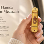 Journey Hamsa Gold Car Mezuzah mezuzah cover held upright in one hand, showing a brown Hamsa hand with a Star of David in its palm, warm gold-colored panels and patterned borders inside a rounded stainless-steel frame beside the product name and illustrated design features in a wide social-sharing graphic for decorative Jewish travel Judaica