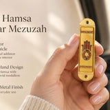 Journey Hamsa Gold Car Mezuzah mezuzah cover held upright in one hand, showing a brown Hamsa hand with a Star of David in its palm, warm gold-colored panels and patterned borders inside a rounded stainless-steel frame beside the product name and illustrated design features in a wide social-sharing graphic for decorative Jewish travel Judaica