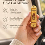 Hand holding the Journey Hamsa Gold Car Mezuzah mezuzah cover inside a vehicle, showing a brown Hamsa hand with a Star of David in its palm, warm gold-colored panels and patterned borders in a rounded stainless-steel frame beside the product name and illustrated features for this decorative Jewish travel Judaica piece