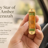 Journey Star of David Amber Car Mezuzah mezuzah cover held upright in one hand, showing an amber orange patterned face, central Star of David, green accent panels and Hebrew Shin inside a rounded gold-colored metal frame beside the product name and illustrated design features in a wide social-sharing graphic for decorative Jewish travel Judaica