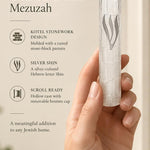 Kotel Stonework Clear Silver Shin Mezuzah mezuzah cover held in one hand beside its product name and illustrated features, with a clear plastic body, molded stone-block texture and an elongated silver-colored Hebrew Shin above the rounded bottom closure clearly visible in a close view of the molded texture and Hebrew design