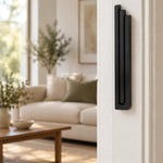 Large Modern Black Pyramid Mezuzah mounted vertically on a white interior doorpost, where its deep matte black aluminum mezuzah cover and three graduated bars create a contemporary Judaica accent with clean geometric lines against the pale doorframe