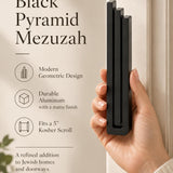 Hand holding the Large Modern Black Pyramid Mezuzah upright, revealing its deep matte black aluminum mezuzah cover, slender three-bar Pyramid design and graduated top beside illustrated product features for contemporary Jewish home Judaica