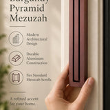 Large Modern Burgundy Pyramid Mezuzah held beside a doorpost, with the muted burgundy wine-red aluminum mezuzah cover shown close enough to reveal its three stepped bars and rounded lower edge alongside product-name and design callouts for this contemporary Judaica piece