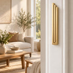 Large Modern Gold Pyramid Mezuzah mounted vertically on a white interior doorpost, where its warm metallic gold aluminum mezuzah cover and three graduated bars create a contemporary Judaica accent with clean geometric lines against the pale doorframe
