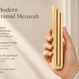 Large Modern Gold Pyramid Mezuzah pictured in hand as a warm metallic gold aluminum mezuzah cover with three graduated bars and a contemporary stepped design, alongside its name and illustrated product features in a wide social-sharing image