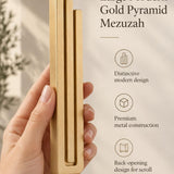 Hand holding the Large Modern Gold Pyramid Mezuzah upright, revealing its warm metallic gold aluminum mezuzah cover, slender three-bar Pyramid design and graduated top beside illustrated product features for contemporary Jewish home Judaica