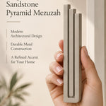 A hand presents the Large Modern Sandstone Pyramid Mezuzah with its warm taupe sandstone aluminum mezuzah cover facing forward, highlighting the clean graduated bars and geometric vertical profile beside design illustrations for a contemporary Jewish doorway accent
