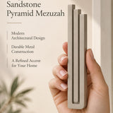 A hand presents the Large Modern Sandstone Pyramid Mezuzah with its warm taupe sandstone aluminum mezuzah cover facing forward, highlighting the clean graduated bars and geometric vertical profile beside design illustrations for a contemporary Jewish doorway accent