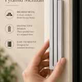 Large Modern Silver Pyramid Mezuzah held beside a doorpost, with the softly brushed silver aluminum mezuzah cover shown close enough to reveal its three stepped bars and rounded lower edge alongside product-name and design callouts for this contemporary Judaica piece