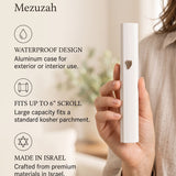 holding the large modern white aluminum outdoor mezuzah case indoors, showing its raised Hebrew Shin beside graphic callouts for waterproof use, a scroll up to six inches and Israeli origin