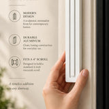 Large Modern White Pyramid Mezuzah held beside a doorpost, with the smooth matte white aluminum mezuzah cover shown close enough to reveal its three stepped bars and rounded lower edge alongside product-name and design callouts for this minimalist Judaica piece
