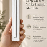 Hand holding the Large Modern White Pyramid Mezuzah upright, revealing its smooth matte white aluminum mezuzah cover, slender three-bar Pyramid design and graduated top beside illustrated product features for minimalist Jewish home Judaica