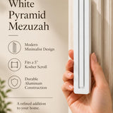 A hand presents the Large Modern White Pyramid Mezuzah with its smooth matte white aluminum mezuzah cover facing forward, highlighting the clean graduated bars and geometric vertical profile beside design illustrations for a minimalist Jewish doorway accent
