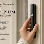 holding a large black aluminum outdoor mezuzah case against a pale front doorpost with its silver Hebrew Shin facing forward, while the graphic highlights waterproof aluminum, six-inch scroll compatibility and Israeli origin