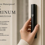 holding a large black aluminum outdoor mezuzah case against a pale front doorpost with its silver Hebrew Shin facing forward, while the graphic highlights waterproof aluminum, six-inch scroll compatibility and Israeli origin