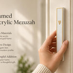 A person holding a Lumen white acrylic mezuzah with gold-toned frame and Hebrew Shin letter.
