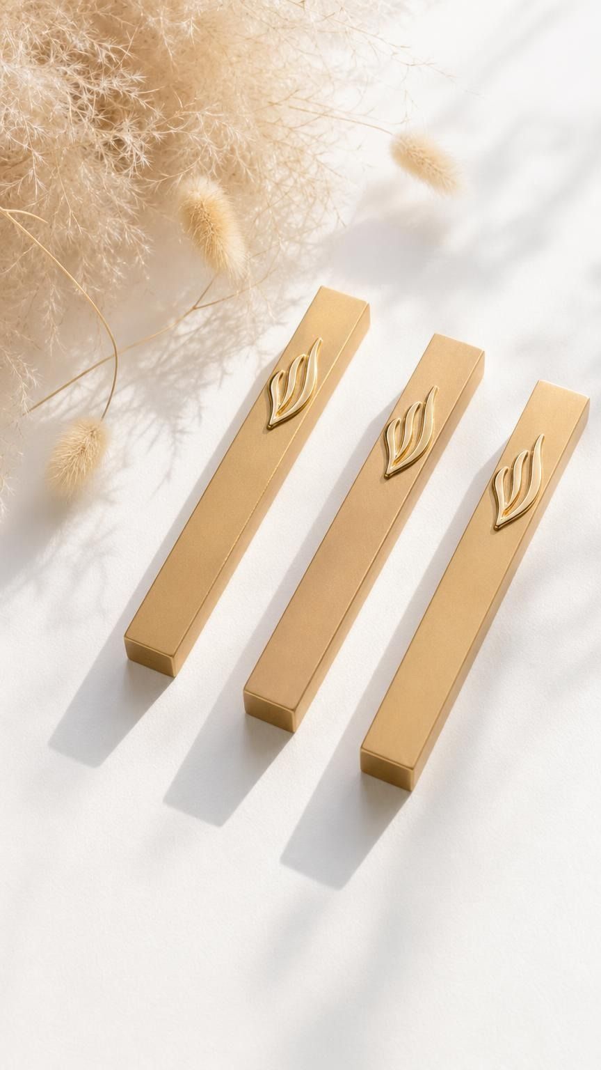 Premium gold mezuzah case with silver accents and minimalist rectangular design, displayed on a clean white surface with pampas flowers