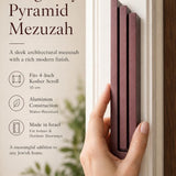 Individual holding the exact modern burgundy pyramid mezuzah at realistic scale, with space for editorial text, emphasizing its precise dimensions and design features.