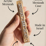 Person holding Shema Mezuzah with curvy arrows indicating placement and features, light background matching product tone.