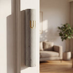 Gray cement Mezuzah with gold accents mounted on a doorframe, with visible screws and a matching room decor, high resolution.