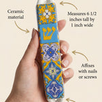 Person holding a ceramic Portugal mezuzah, showcasing the product's size and design details with a clean background.