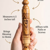 Person holding olive wood mezuzah, emphasizing craftsmanship and material details in a clean layout.