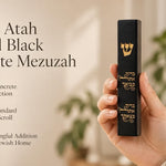 Close-up of a hand holding a black concrete mezuzah case featuring a gold Shin and Hebrew blessing text.