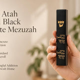 Close-up of a hand holding a black concrete mezuzah case featuring a gold Shin and Hebrew blessing text.