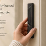 A hand holding a modern black concrete mezuzah case featuring an embossed gold Hebrew Shin letter.