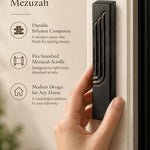 Person holding a matte black concrete mezuzah case featuring an embossed gold-edged Hebrew Shin letter.