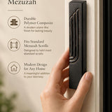 Person holding a matte black concrete mezuzah case featuring an embossed gold-edged Hebrew Shin letter.