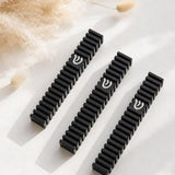 Three Modern Black Steps aluminum mezuzah cases arranged on a warm neutral surface with dried florals, showing the repeated architectural black fins and contrasting silver Hebrew Shin on each modern Israeli mezuzah