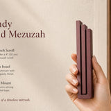 Person holding the Modern Burgundy Pyramid Mezuzah, made of aluminum with a deep red finish, showcasing its architectural stepped design