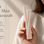 Hand holding a silver and pink aluminum mezuzah case with screw cap, suitable for outdoor doorways, shown in a natural, balanced composition.