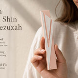 Hand holding a silver and pink aluminum mezuzah case with screw cap, suitable for outdoor doorways, shown in a natural, balanced composition.
