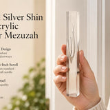 A hand holding a modern transparent acrylic mezuzah case with a polished silver Shin design for indoor or outdoor use.
