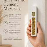 Hand holding a Modern Gold Crystal Inlay White Cement Mezuzah case in a warm neutral interior, showing the slim white cement profile, raised gold Shin, and dense vertical gold crystal and glass inlay with champagne and reflective golden tones