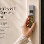 Hand holding a Modern Golden Amber Crystal Inlay Gray Cement Mezuzah case with a raised silver-tone Shin and warm golden amber crystal and glass pieces, showing the contrast between the cool gray cement body and rich honey, bronze, and amber-toned inlay